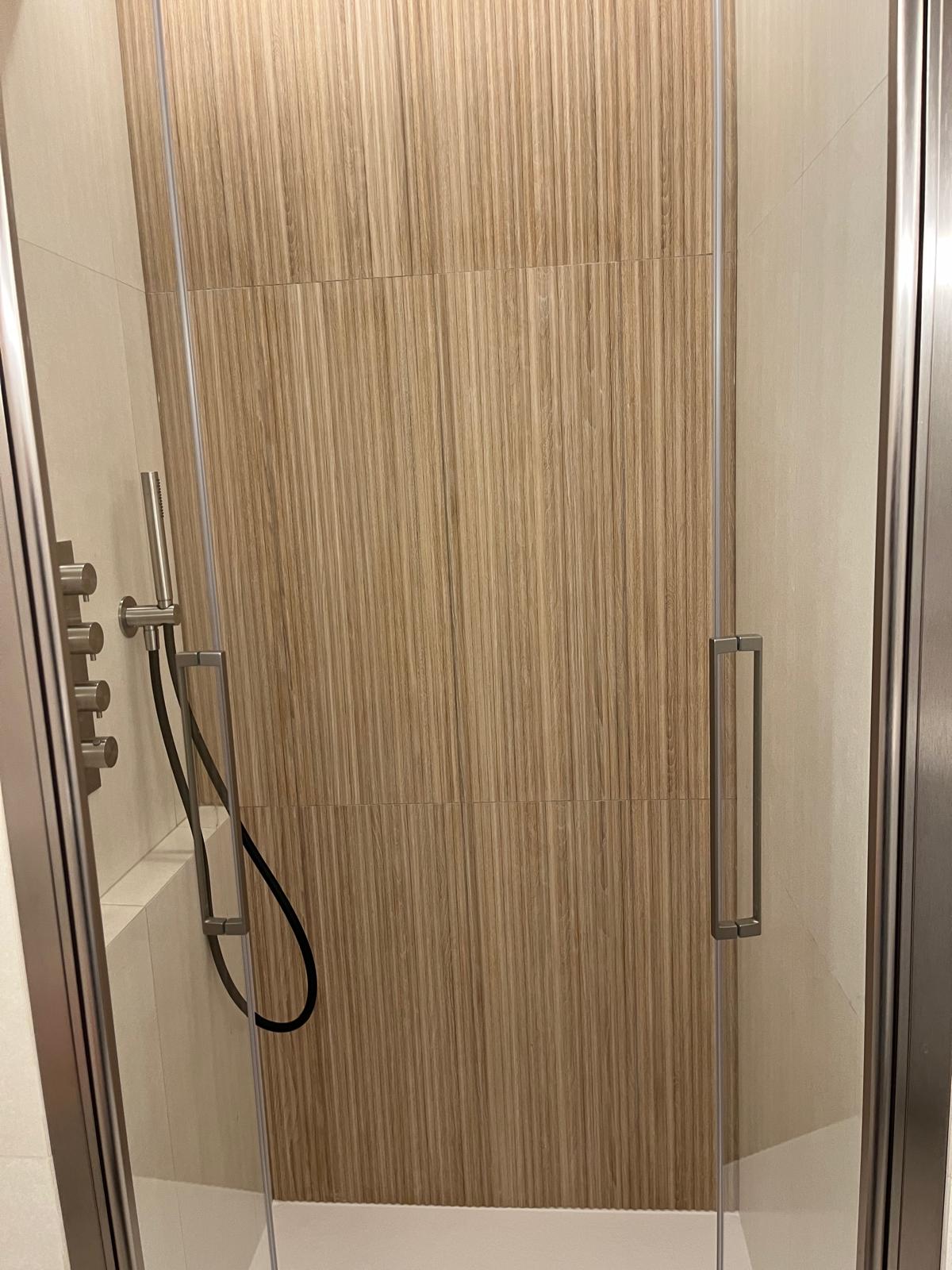 Vue de face de la douche vitrée, avec revêtement à motif bois et colonne chromée — chantier CAREN